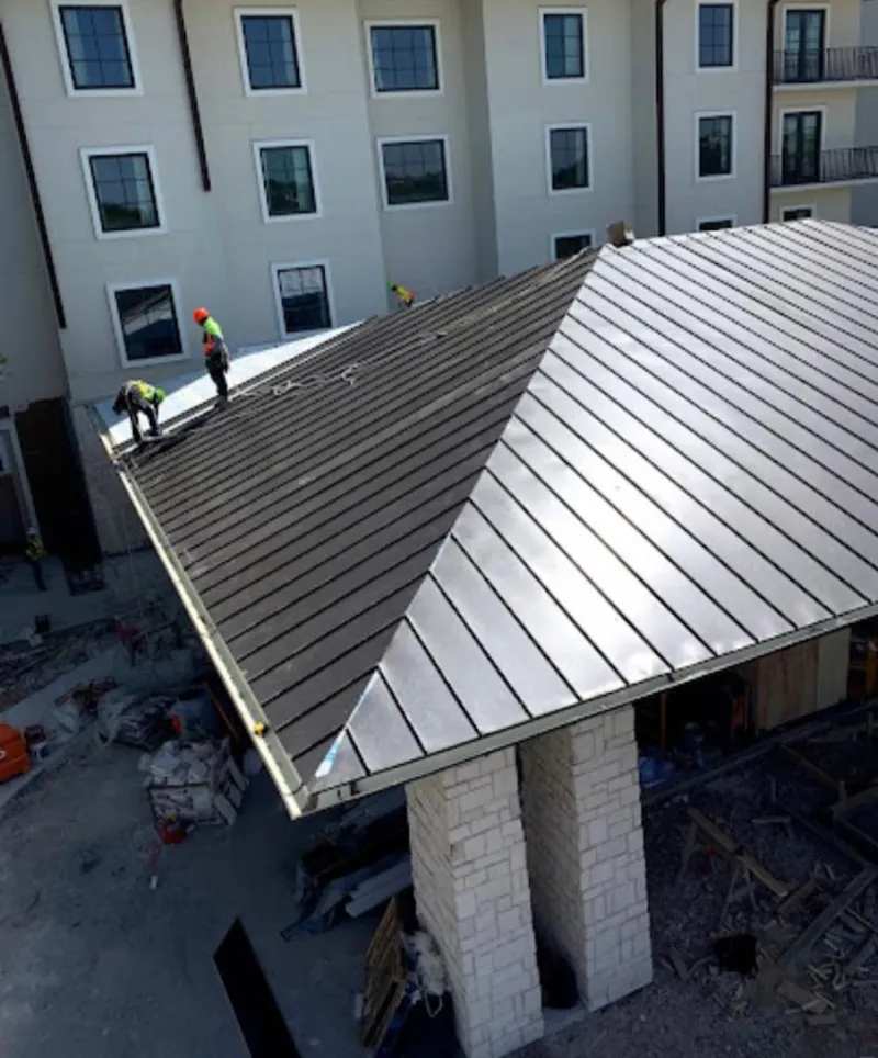 Crew installing standing seam metal roof panels on a commercial project in Milford